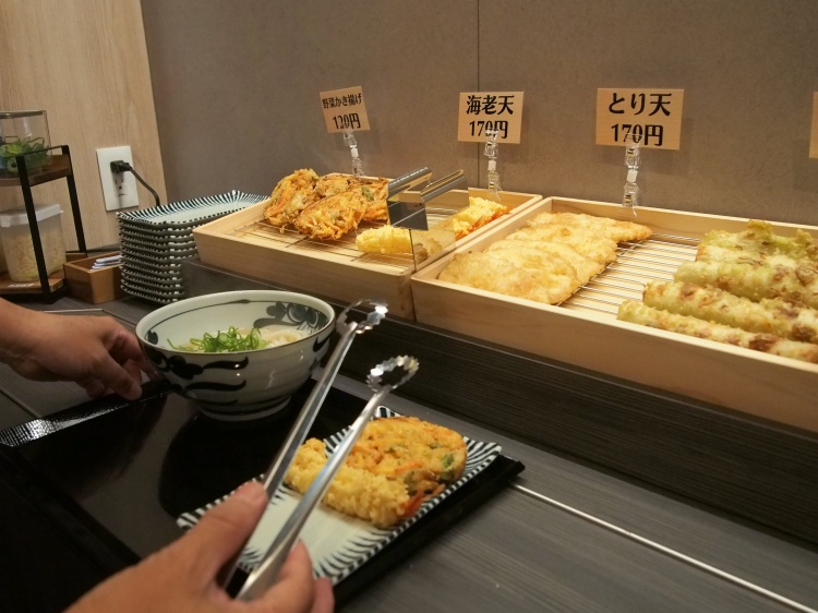 PSPO（ピースポ）愛大前店セルフうどんの天ぷらトッピングを取る様子
